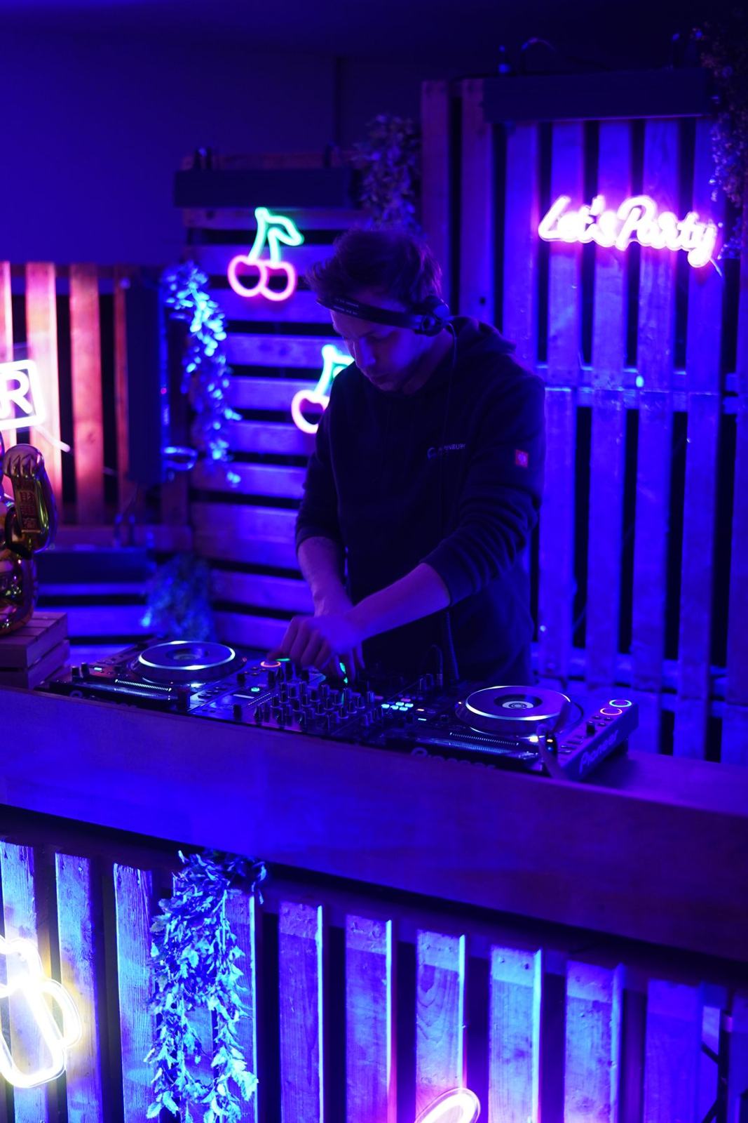 Milo Sava at the decks in blue light under neon cherries